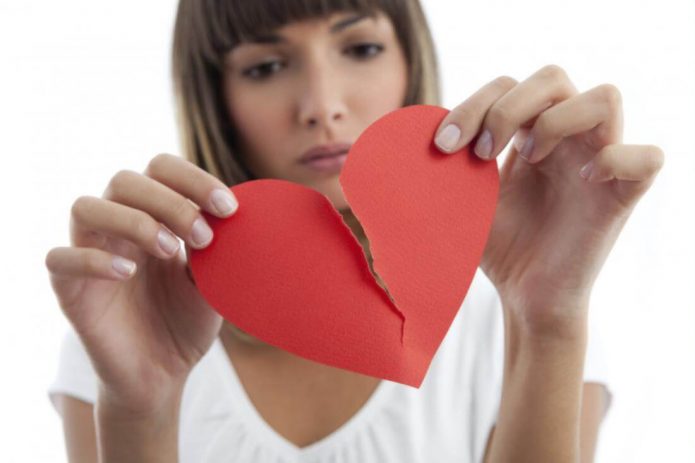 Девушка держит две половинки бумажного разорванного сердца