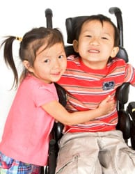 Girl hugging a little boy in a wheel chair.